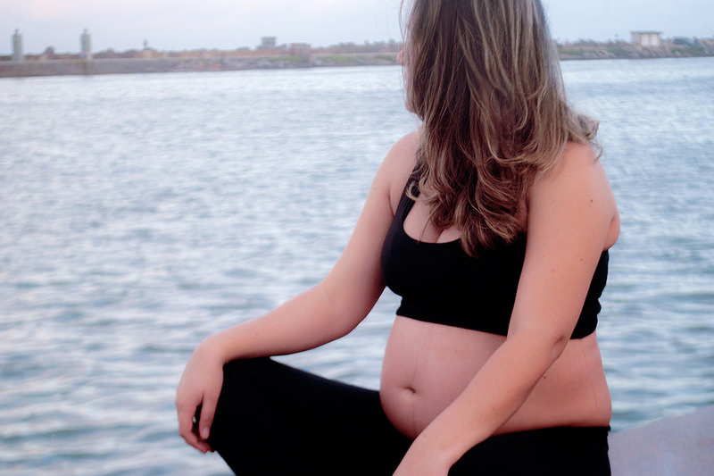 Photo of a pregnant lady sitting on a wall next to a river