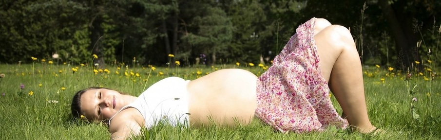 Photo of a pregnant lady lying on the grass with her eyes closed, relaxing
